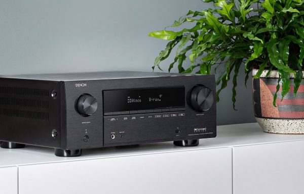 Closeup of Denon AVC-X3700H AV Receiver displaying Atmos and B-Ray on white AV cabinent next to a plant.