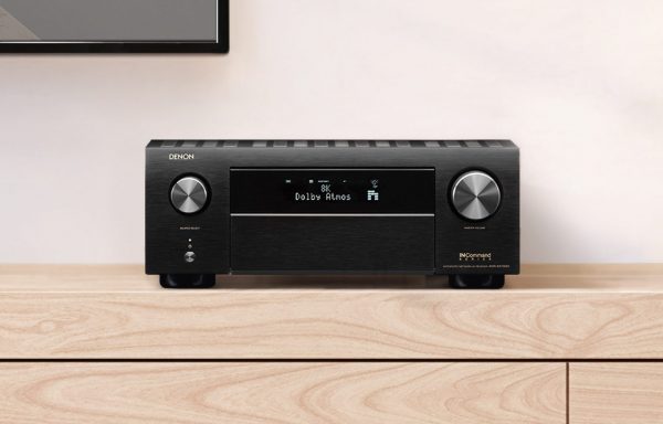 Lifestyle image of Denon AVC-X4700H AV Receiver sitting on cabinent and powered on. Displays 8K and Dolby Atmos on display panel.