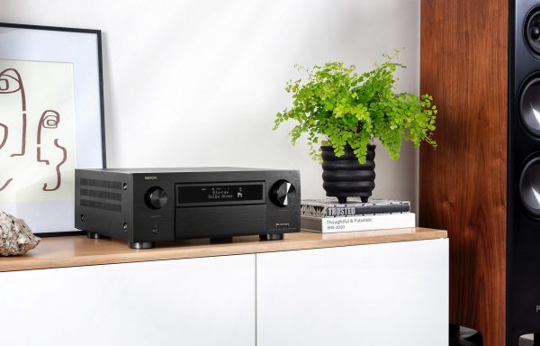 Lifestyle image of Denon AVC-X6700H AV Receiver on bench next to two books with planter.