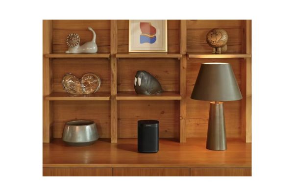 Lifestyle image of black Sonos One SL Smart Speaker sitting on display unit