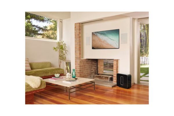 Lifestyle image of Black Sonos Sub Premium Wireless Sub-woofer next to fireplace in open plan living room.