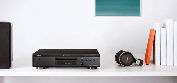 Denon DCD-600 sitting on bench next to headphones and books on right side and speaker on left side of unit.