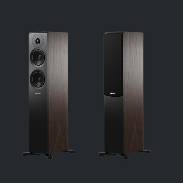 Pair of Dynaudio Emit 30 in walnut on black background, left speaker showing without speaker grill where as one on the right is showing speaker grill that comes as standard.